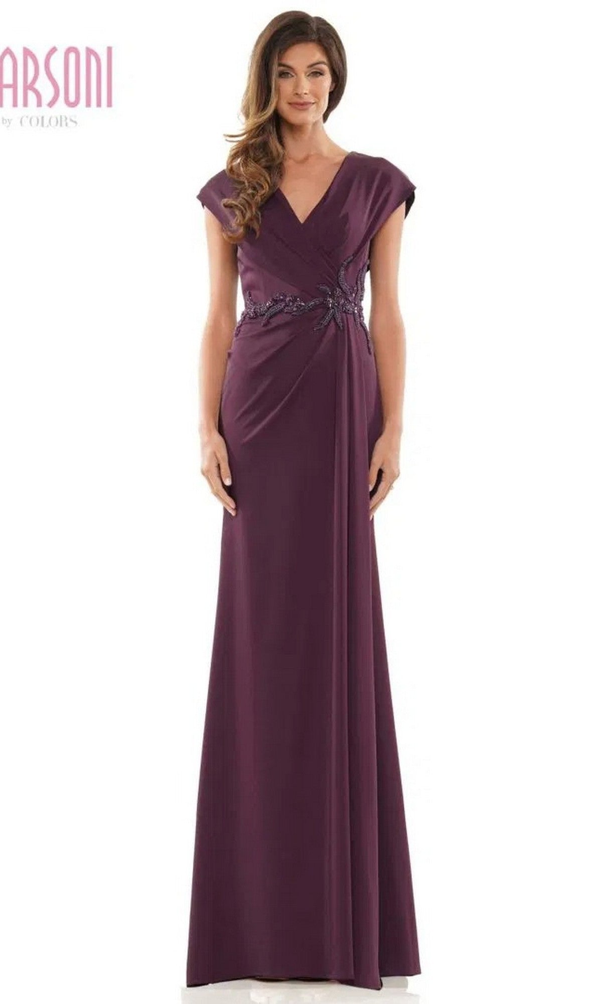 A woman stands against a white background wearing the Marsoni MV1226 long formal dress in eggplant, featuring short sleeves, a V-neckline, and beaded embellishment at the waist.